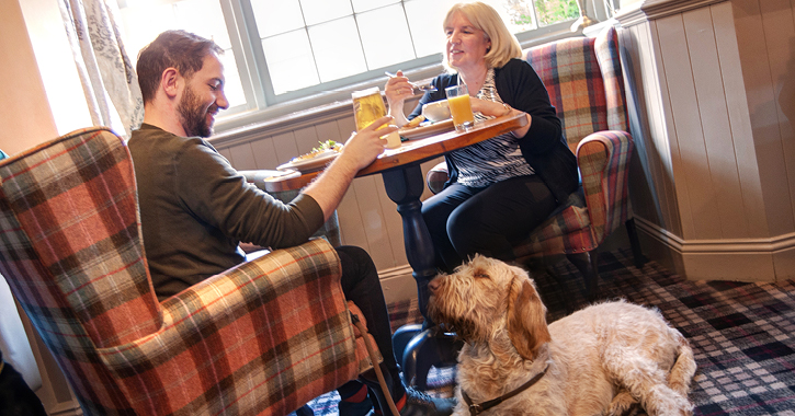 man and woman eating food with a dog sitting next to table in the Kingslodge Inn
